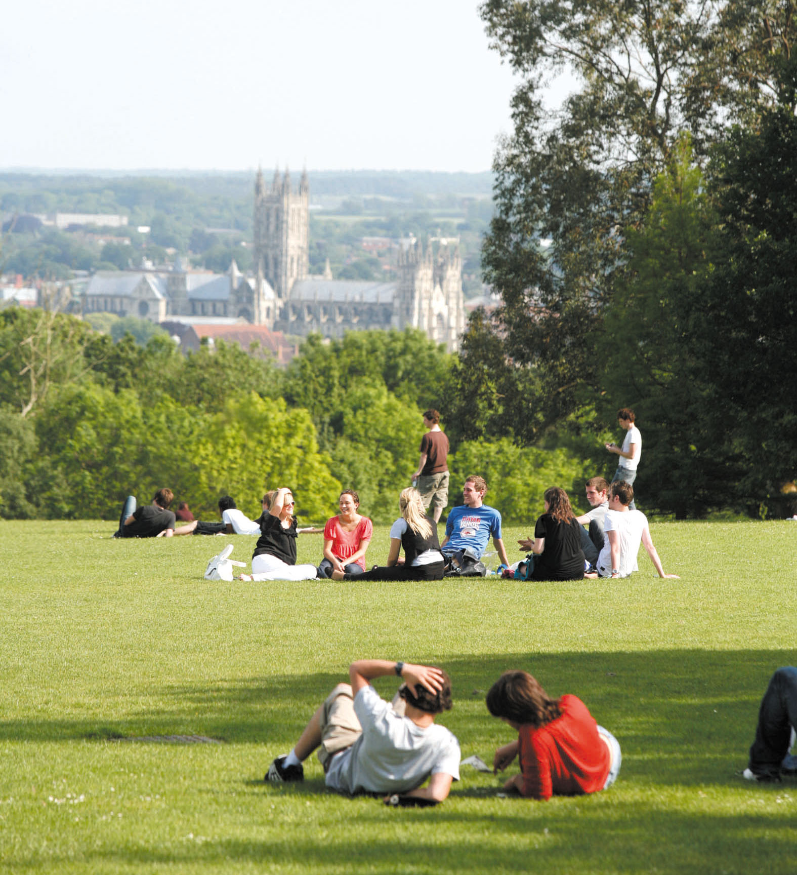 Students sitting on a green lawn with cathedral in the distance