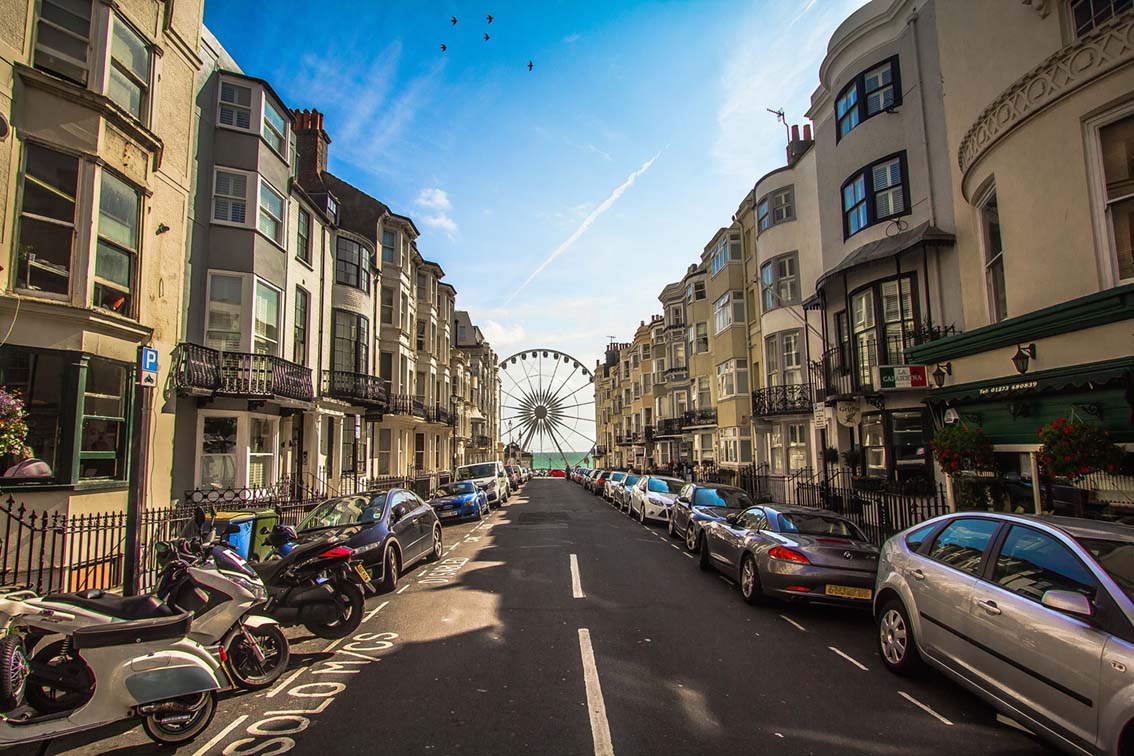 View looking down a street surrounded by buildings with a ferris wheel on the beach at the end