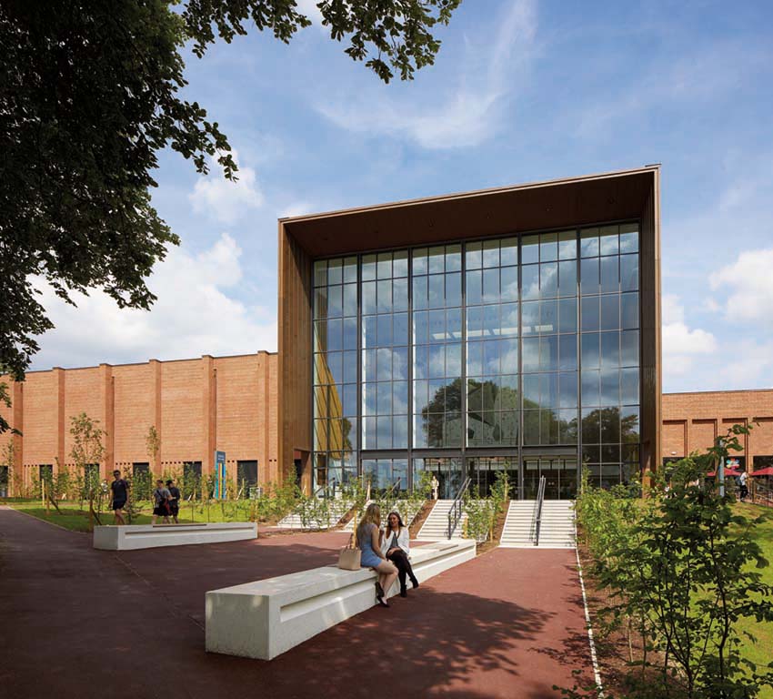 Campus building with large windows reflecting trees and the sky with students in foreground