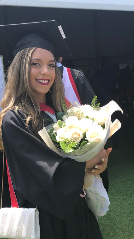 Photo of Nicole smiling, in graduation cap and gown, holding flowers