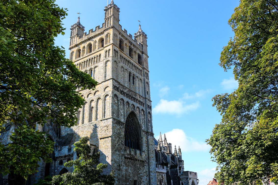 View of Exeter cathedral through trees, looking up toward blue sky