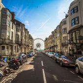 View looking down a street surrounded by buildings with a ferris wheel on the beach at the end