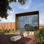 Campus building with large windows reflecting trees and the sky with students in foreground