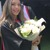 Photo of Nicole smiling, in graduation cap and gown, holding flowers