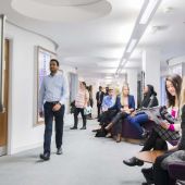 View looking down a hallway with doors on left and students sitting along benches on left