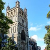 View of Exeter cathedral through trees, looking up toward blue sky